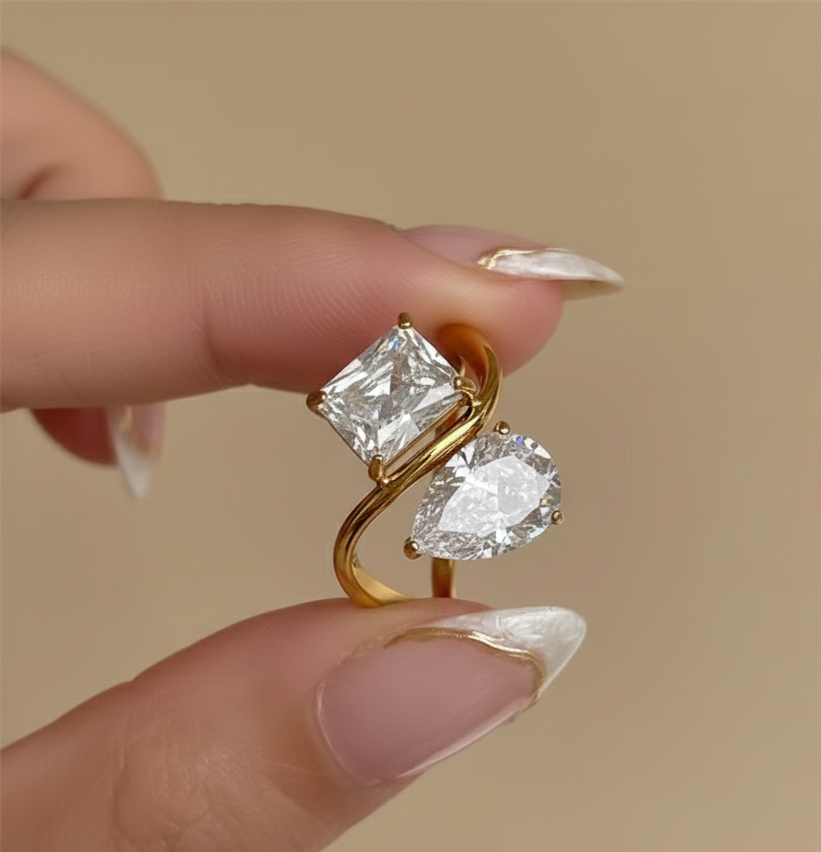 Gold ring with two diamond stones held between fingers against a beige background