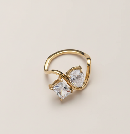 Gold ring with two clear gemstones on a beige background