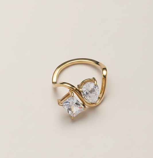 Gold ring with two clear gemstones on a beige background