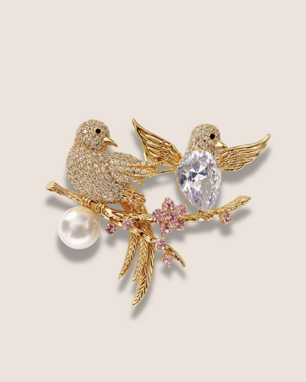 Gold bird brooch with a pearl and gemstones on a beige background