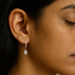 A close-up image of a woman's ear wearing a silver drop earring with a crystal accent.