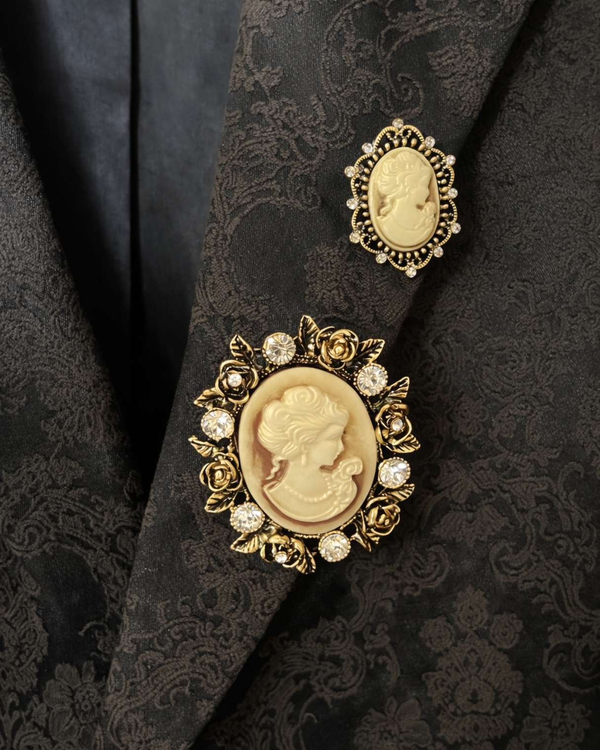 Gold brooches with cameo designs on a black textured fabric background