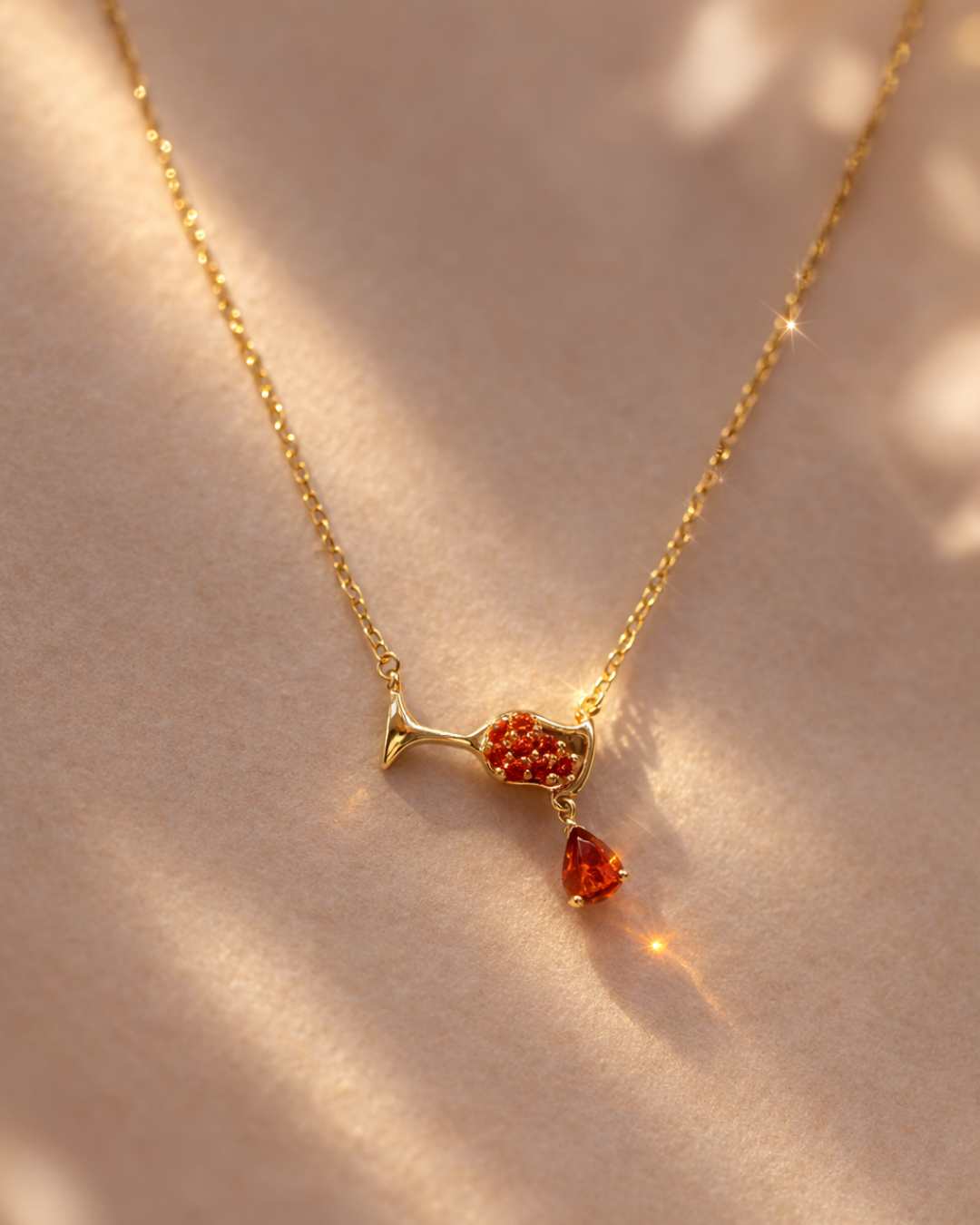Gold necklace with a red gemstone pendant on a beige background