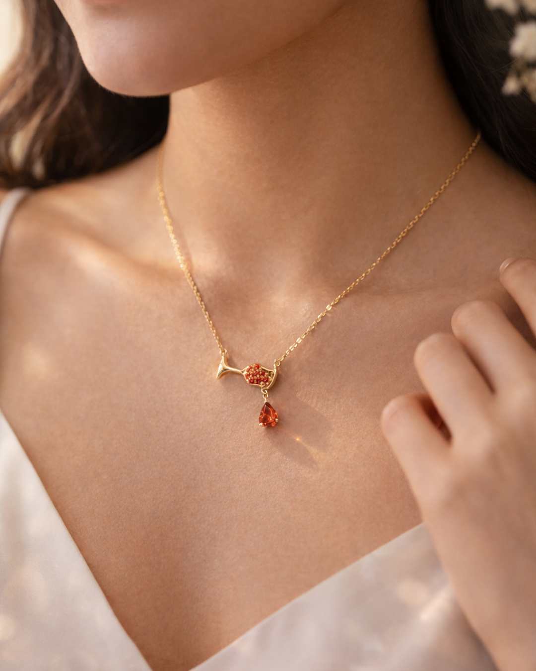 Gold necklace with a pendant featuring red gemstones on a person wearing a white top.